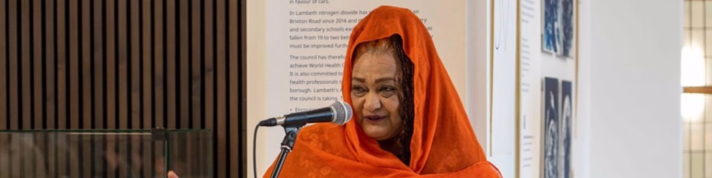 A woman in an orange hijab speaking into a microphone.