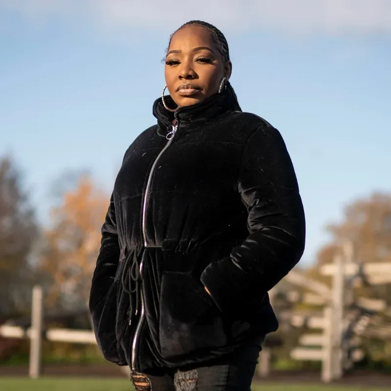 A woman stands tall in the park in a black jacket on a clear day.