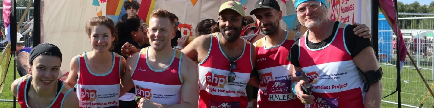 A group of young runners standing in a field before a half-marathon wearing pink branded SHP running vests, all looking happy at the camera