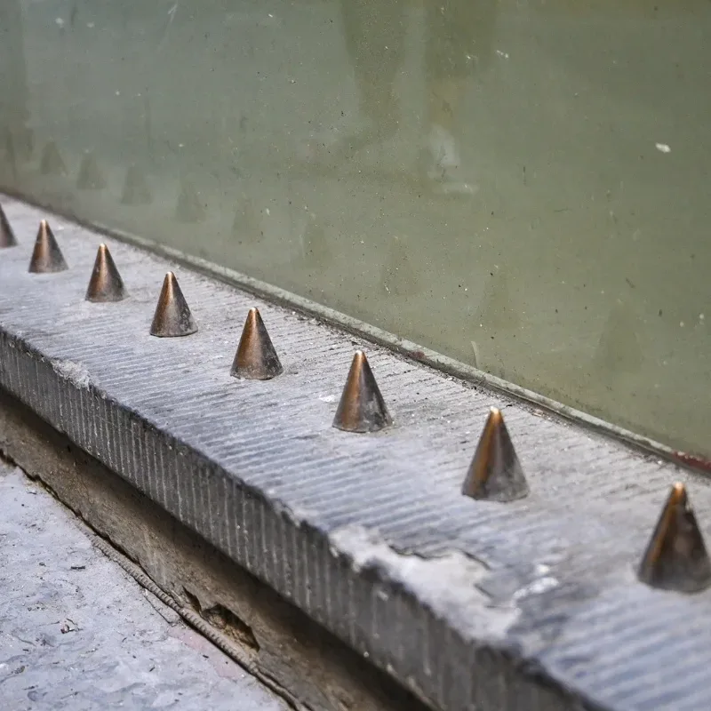 A row of sharp spikes protruding from a wall next to a building.