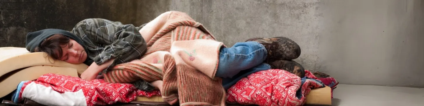Woman rough sleeping in a city, looking cold and trying to sleep