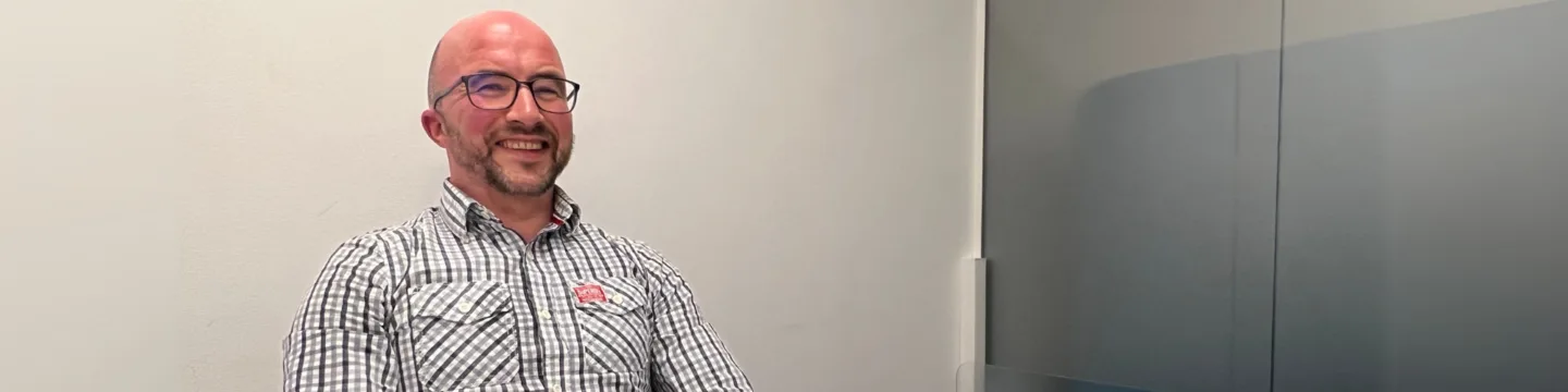 White man with glasses and smart shirt smiles happily at camera
